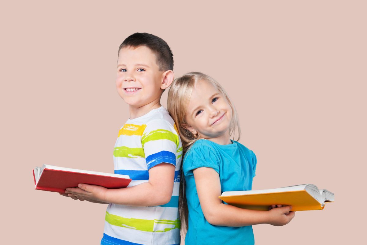 kids leaning back to back from each other holding books to read for summer to bridge the learning gap