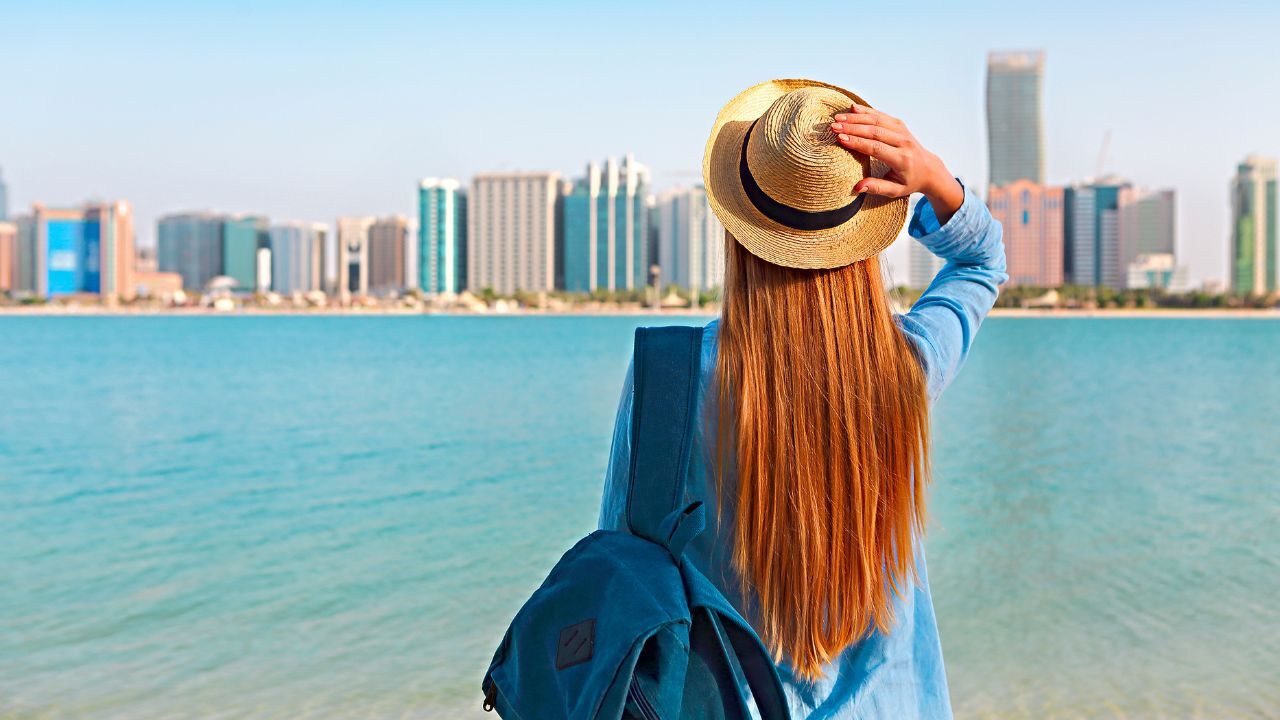 woman abu dhabi Woman with backpack weaing the hat. On the background is panorama of Abu Dhabi