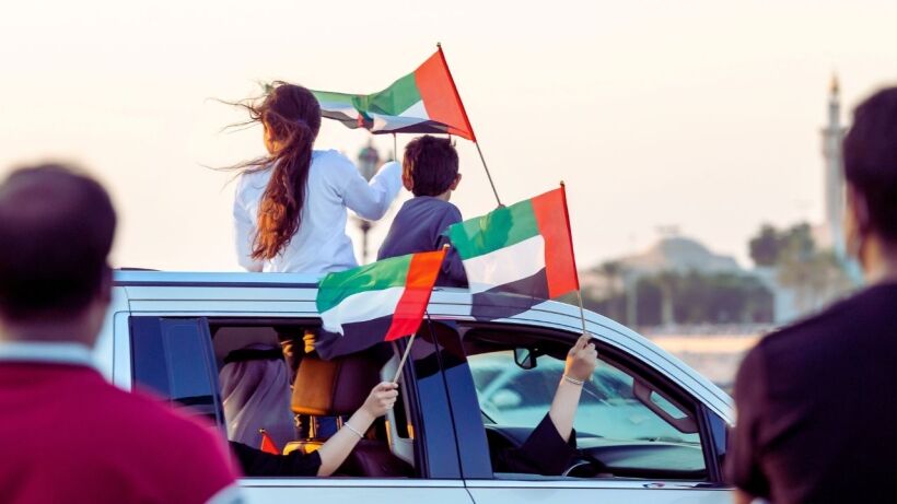 Family celebrating UAE National Day on Corniche. Children with UAE flags