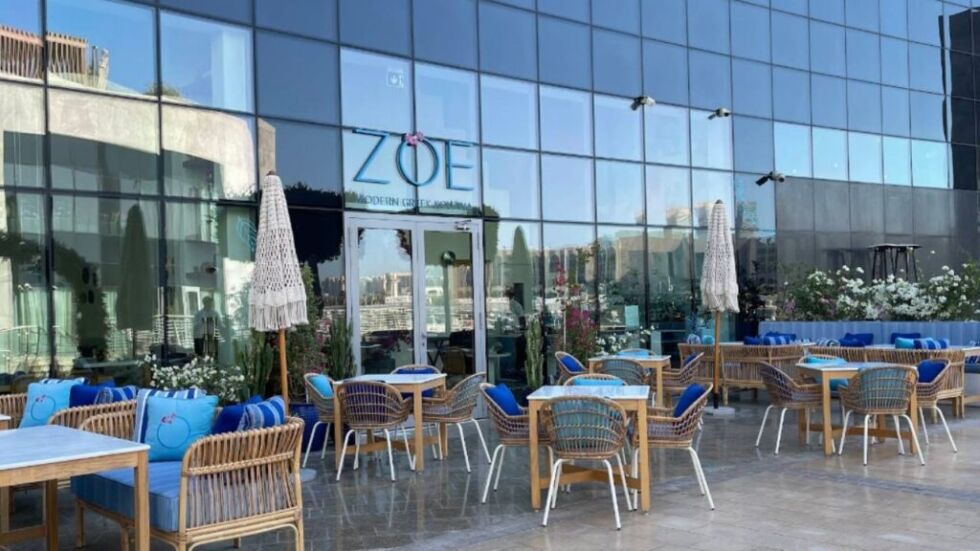 a building with a glass wall and tables and chairs ZOE Modern Greek Kouzina