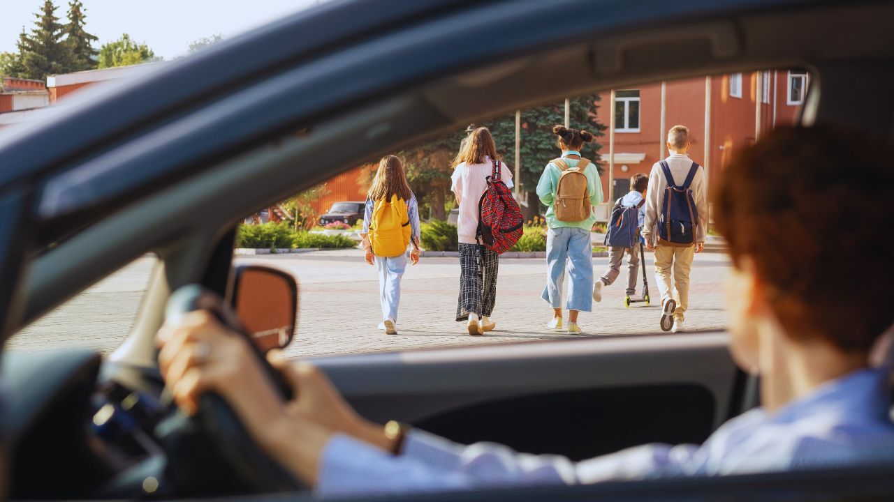 kids going to school (1) Group of schoolkids with backpacks moving along street while young female in car looking at them